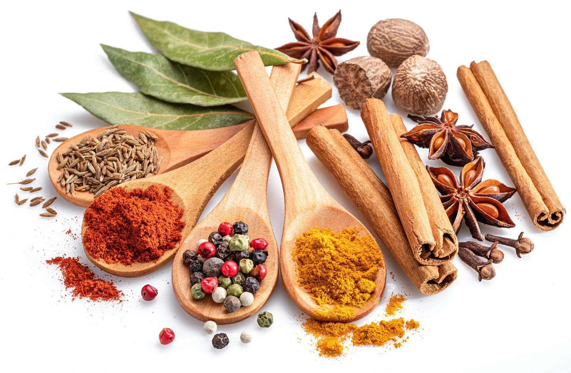 Colorful different seasonings in wooden spoons surrounded with herbs and spices on white background.